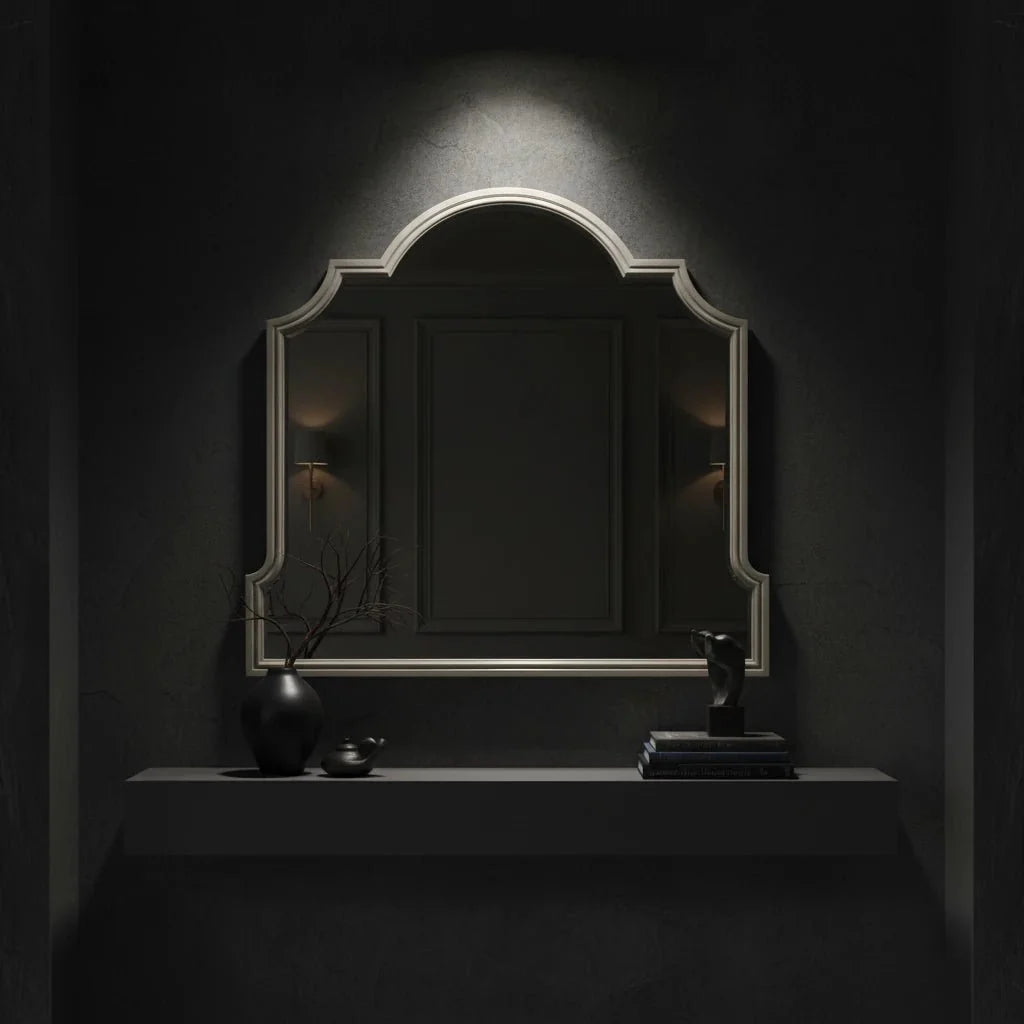 Decorative mirror with a dark frame on a dark wall, illuminated by a spotlight.