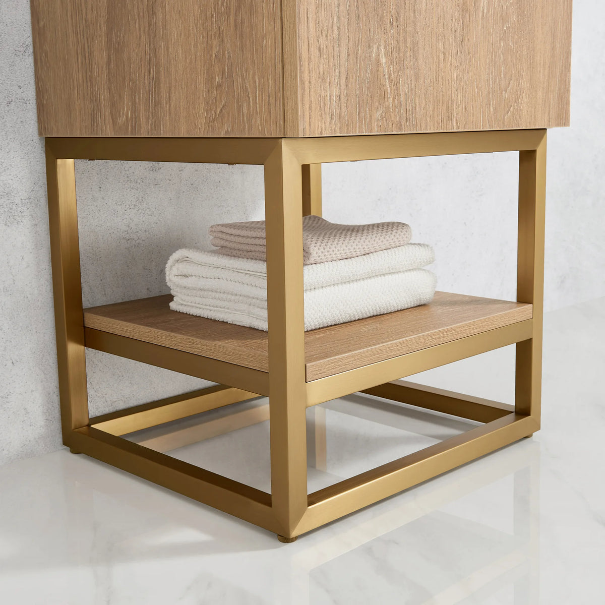 Close-up of the open shelf and Brushed Gold metal base holding folded white towels