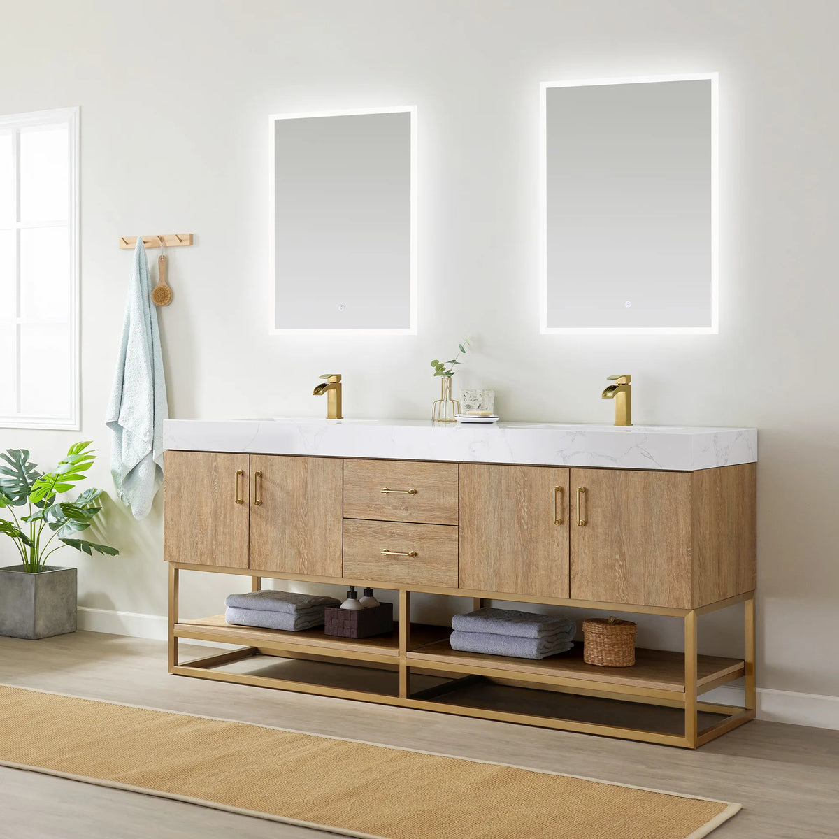 Angled view of the double vanity with LED mirrors, towels on the open shelf, wall hooks, plant and rug