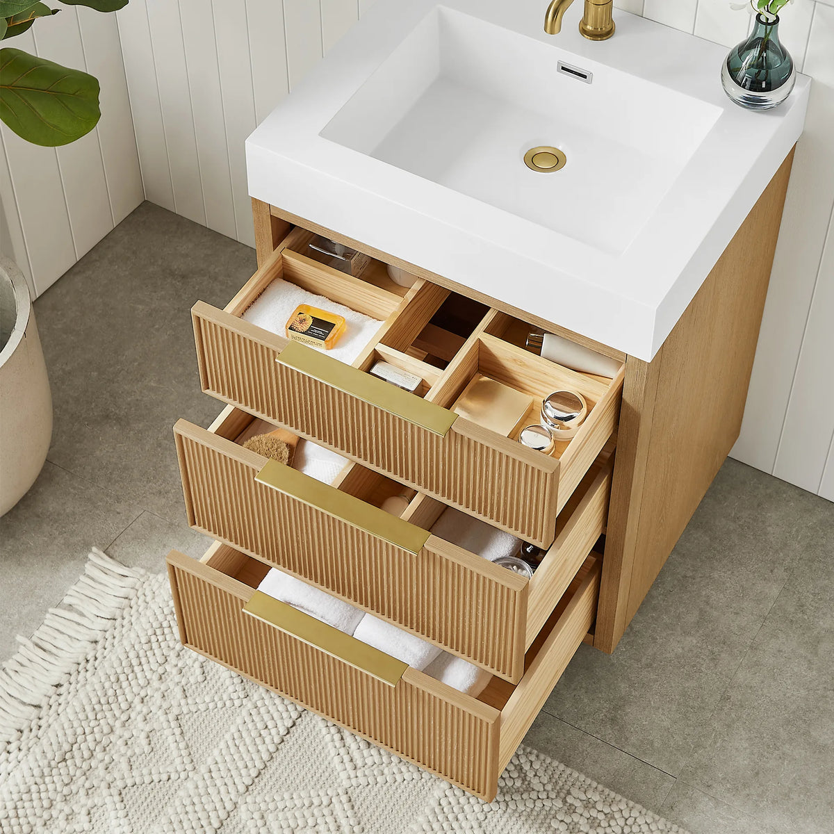 Drawers pulled out on the 24-inch vanity, showing divided interiors and gold pulls, with the white basin above