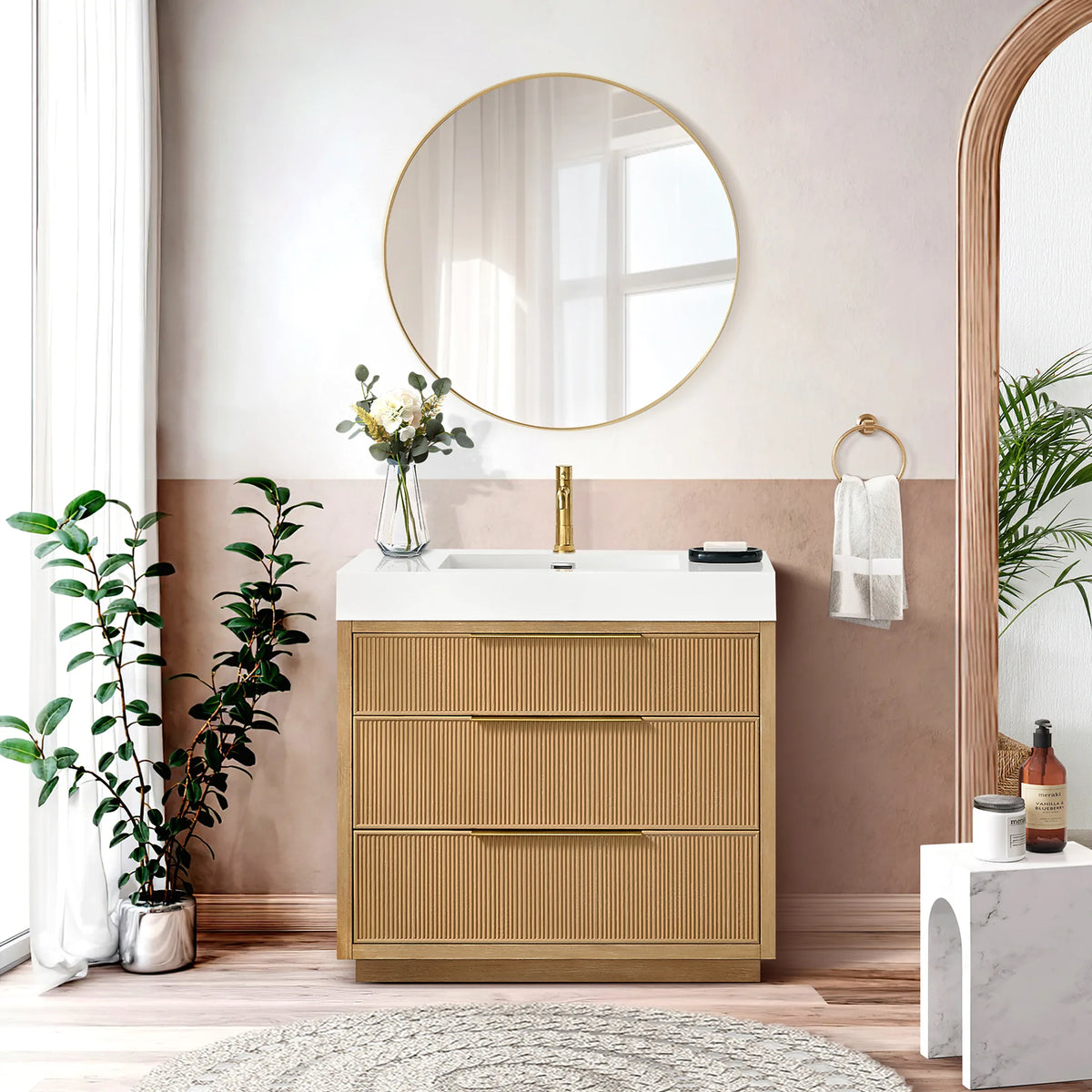 36-inch single vanity against a blush wall under a circular gold mirror, with plants, a towel ring and a white arched stool