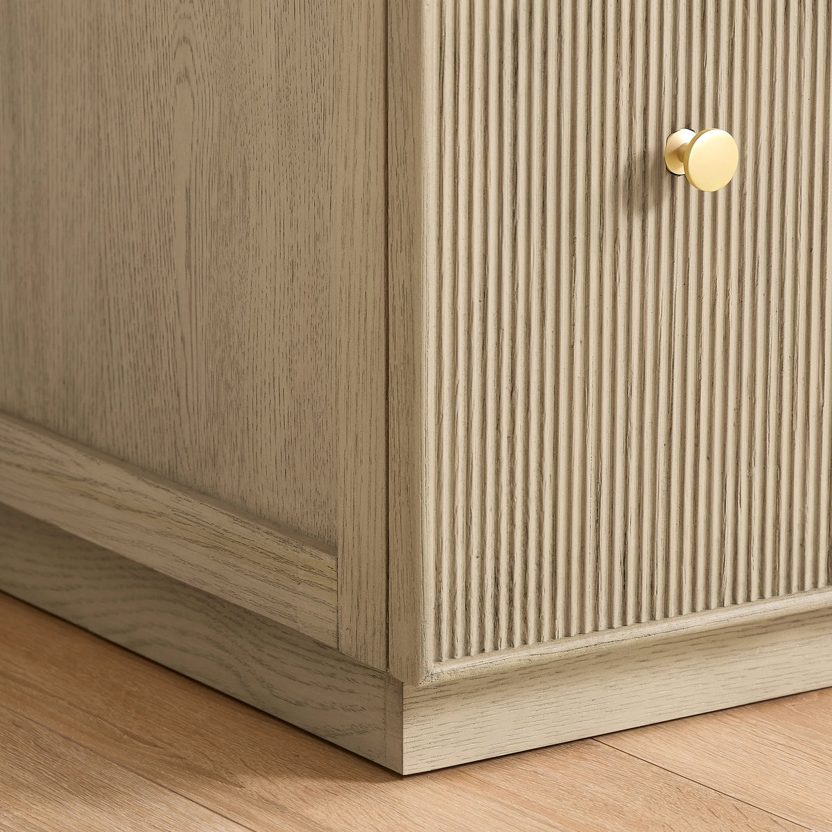Close-up of a textured door front, a Brushed Gold handle and the cabinet base in Aged Natural Oak