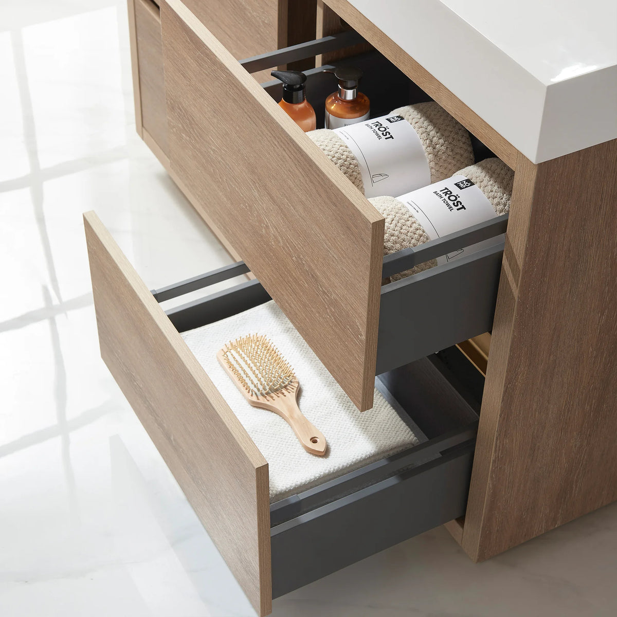 Close-up of open drawers holding towels, a hairbrush and bottles, gray drawer sides