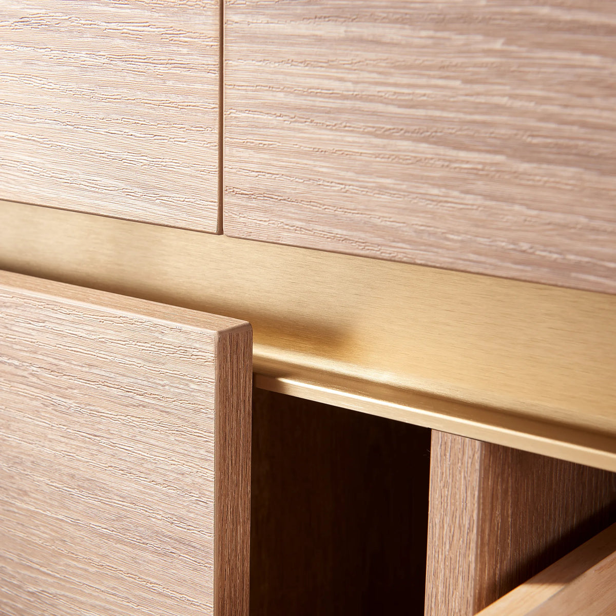 Detail of a brushed gold pull channel between oak fronts, vanity hardware close-up