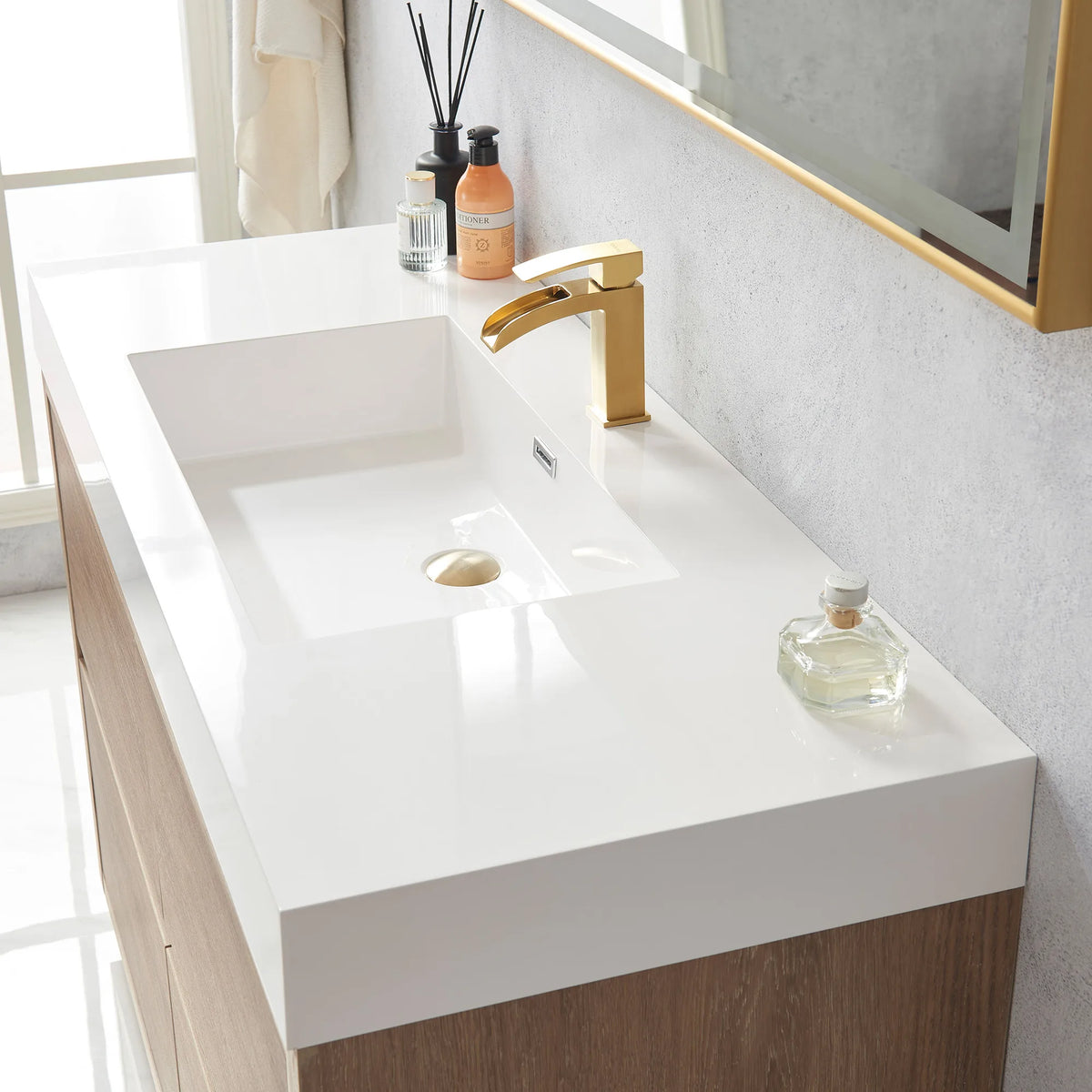 Close-up of the white integrated sink with drain, a small bottle and diffuser, mirror edge at top