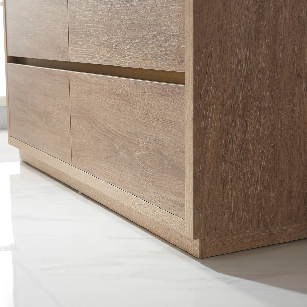Low-angle close-up of oak front panels, gold pull recess and plinth base