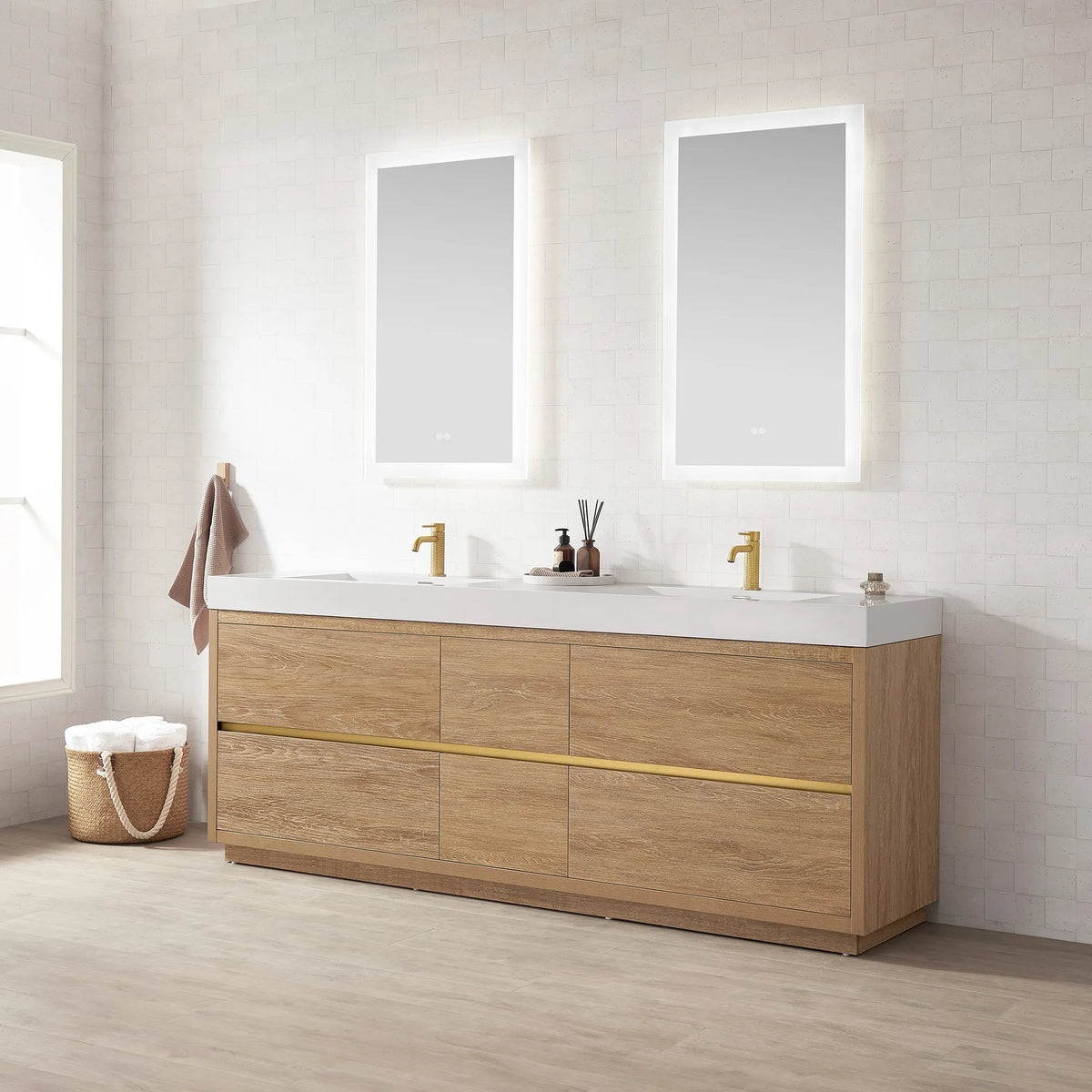 Three-quarter view of the double vanity with mirrors above, window, basket of towels and plank floor