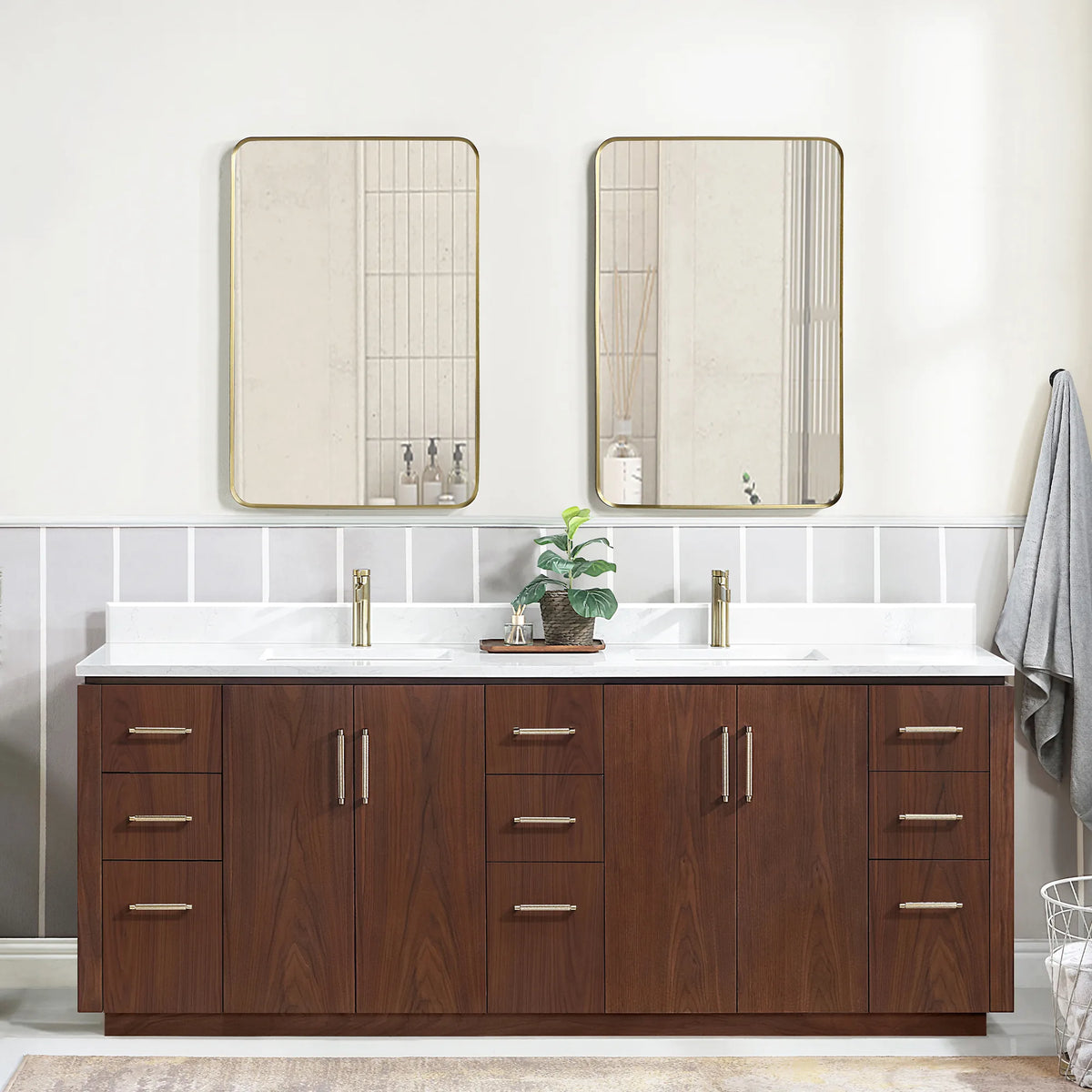 Wide room view of the double vanity with mirrors, a plant at center and a basket at the lower right