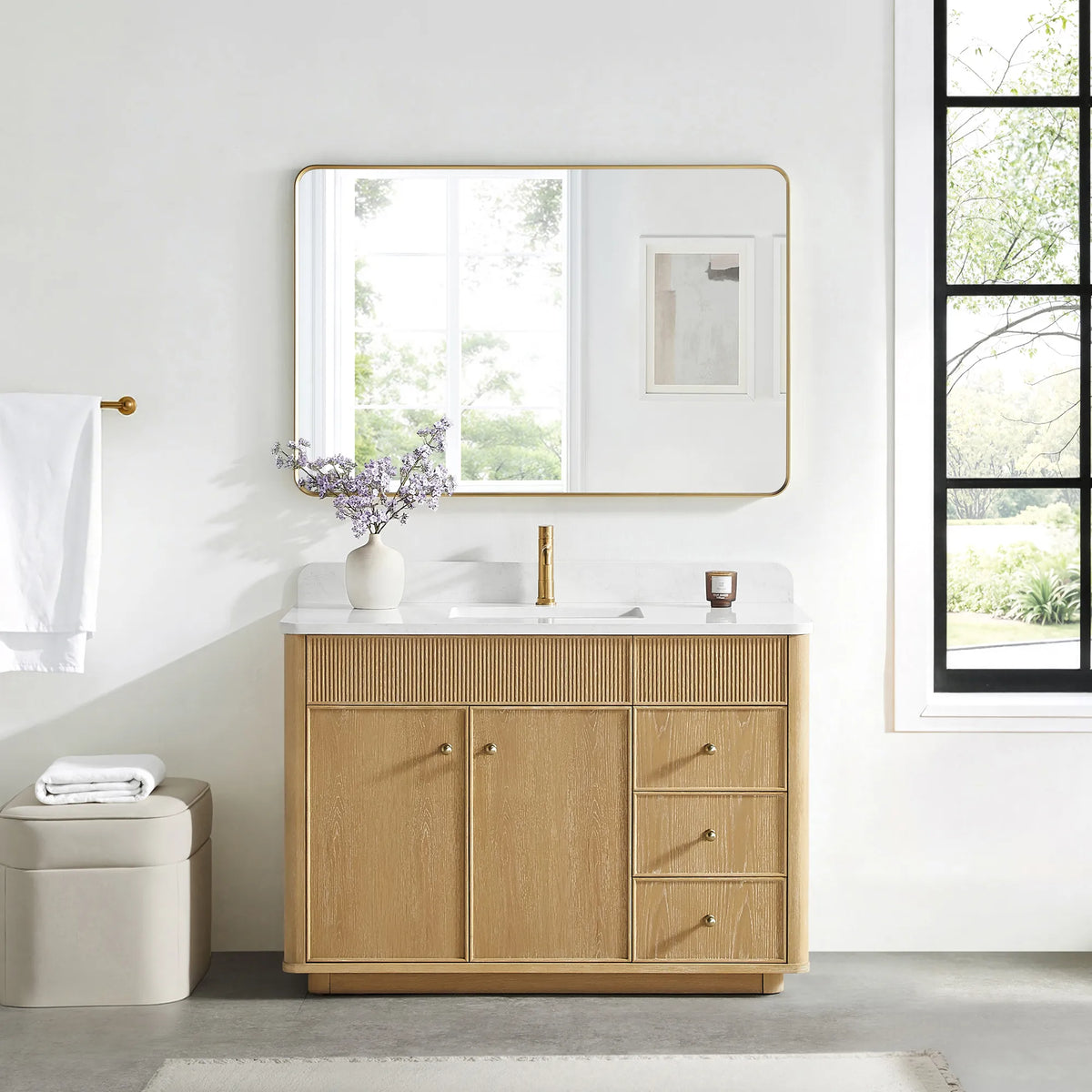 Matching wide rounded-rectangle gold mirror above the Washed Ash Grey vanity in a bathroom with a black-framed window