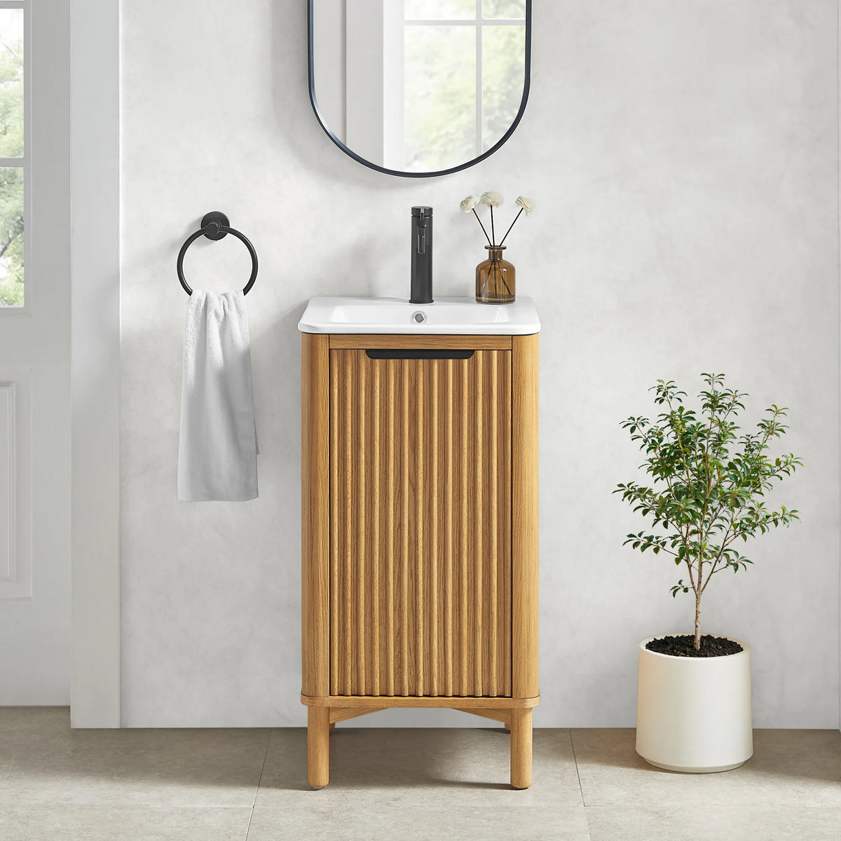 Small bathroom scene for the 18-inch vanity and its matching oval mirror, with a black faucet, towel ring and a potted plant