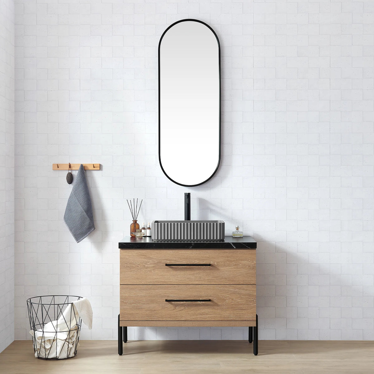 Oval black-framed mirror over the oak vanity, towel on the wall hook, brick tile behind