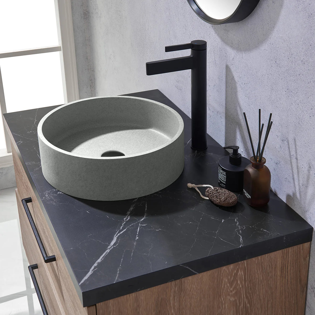 A faucet and the circular concrete vessel on black stone, seen sideways