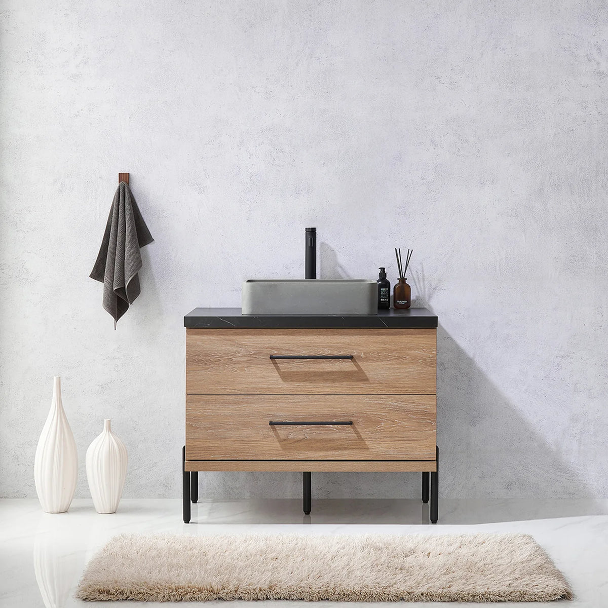 Pale plaster wall, white vases and a hanging towel behind the oak vanity on black legs