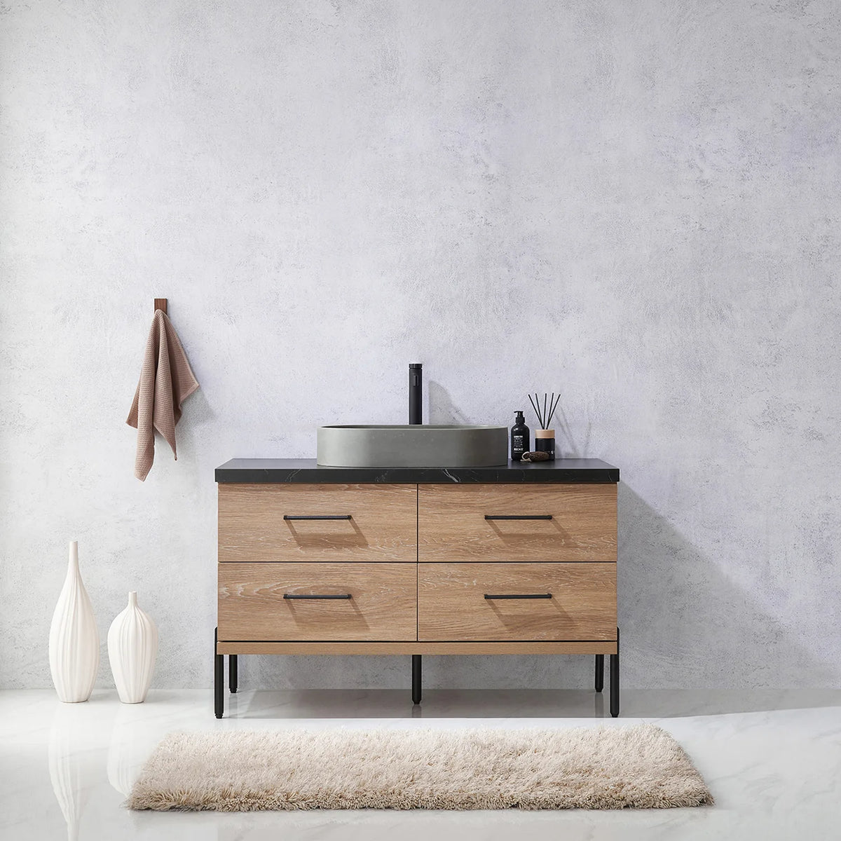 Pale plaster wall, white vases and a hanging towel behind the oak vanity on black legs