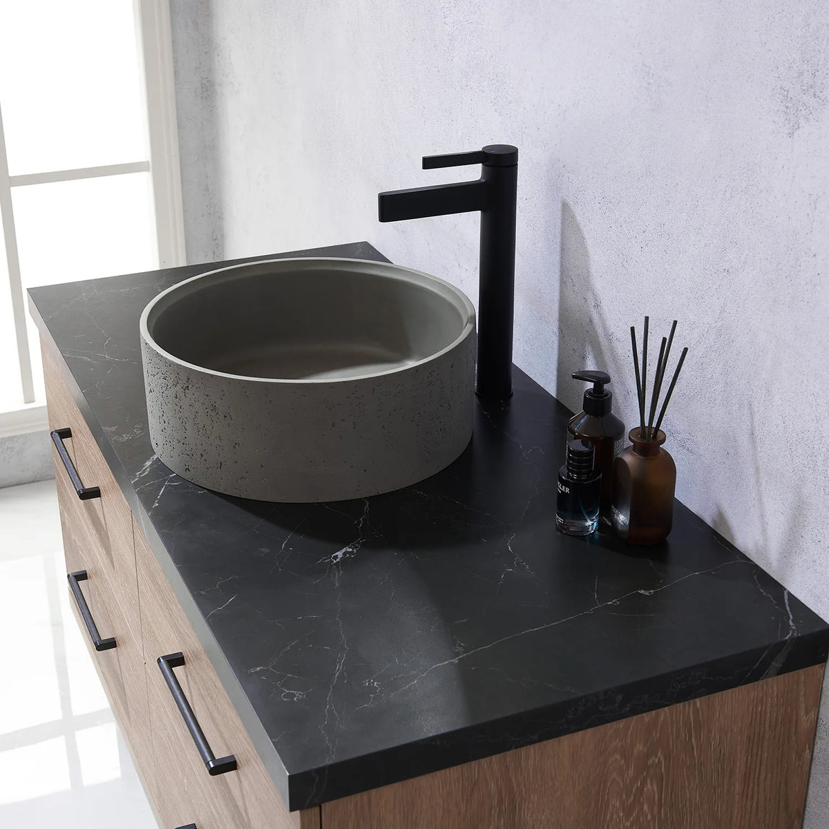 Tall black faucet rising next to the circular concrete vessel on a marbled black surface