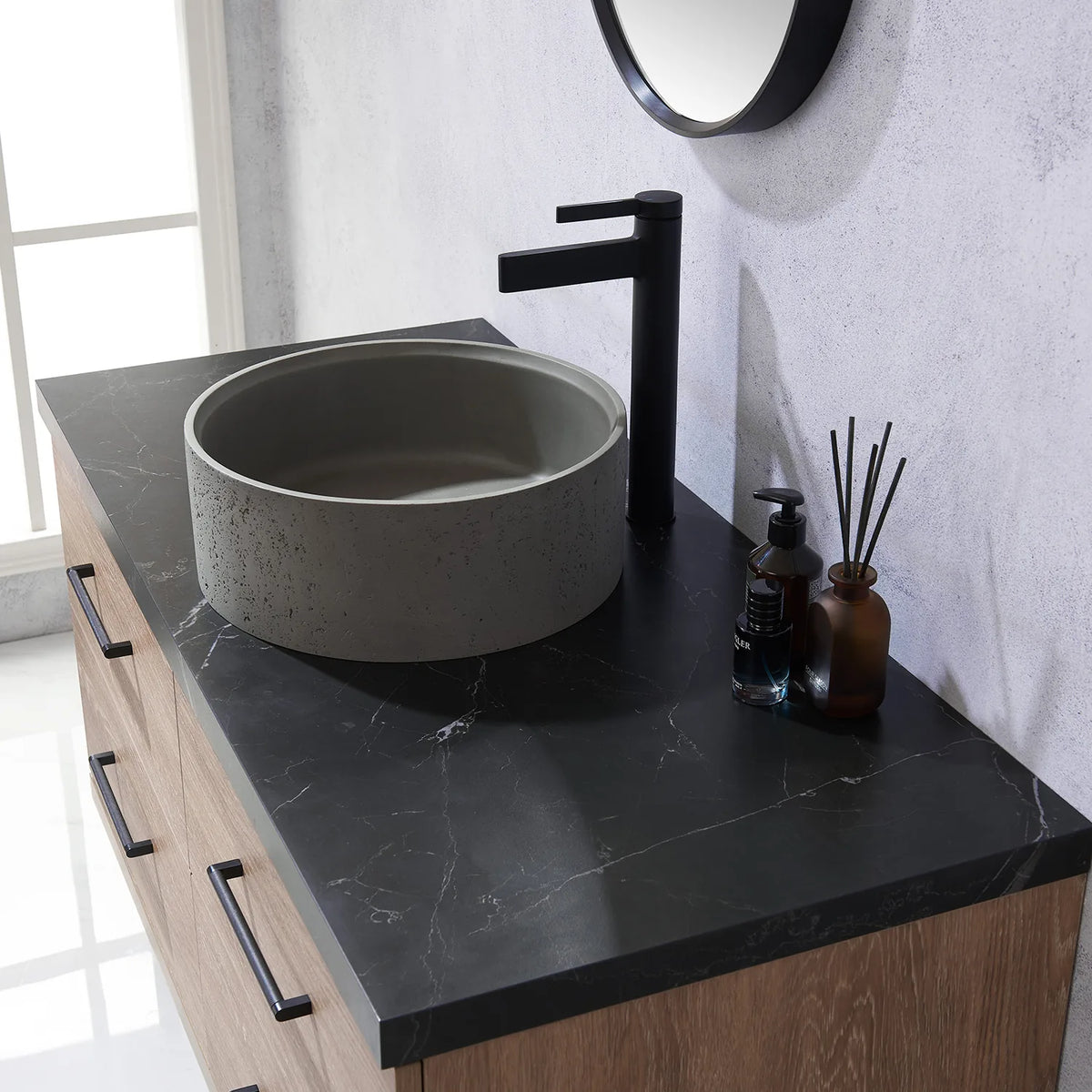 A faucet and the circular concrete vessel on black stone, seen sideways