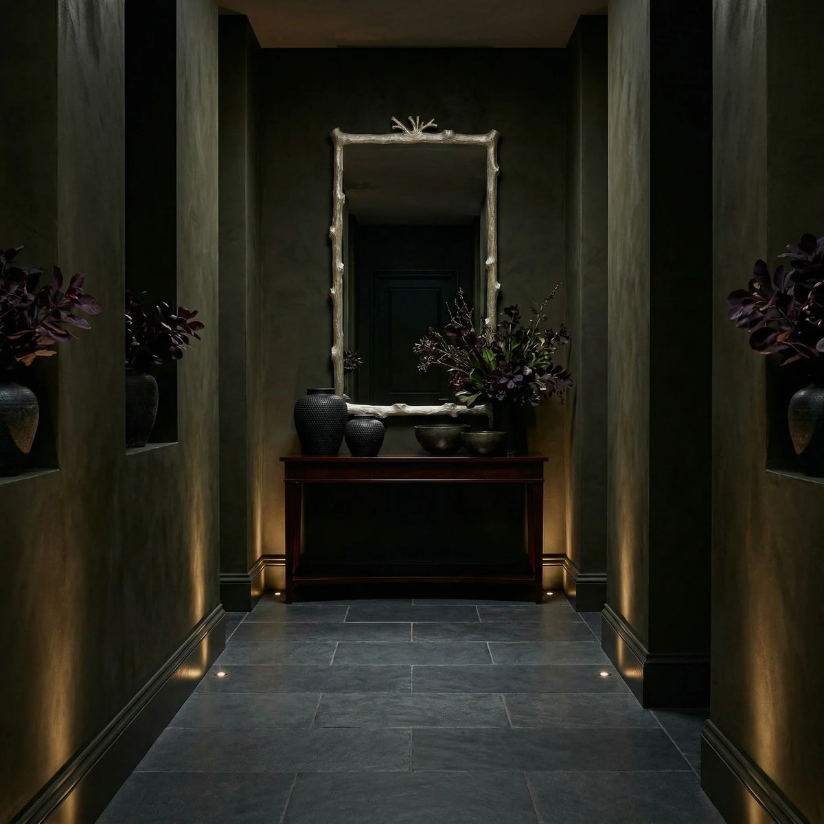 Rectangular Twig Mirror by Ambella Home with soft gold leaf finish and sculptural branch detail, displayed above a console in a dramatic dark hallway