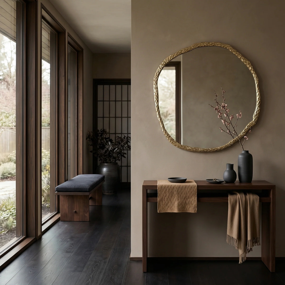 Modern interior with a round mirror, wooden console table, and bench by large windows.