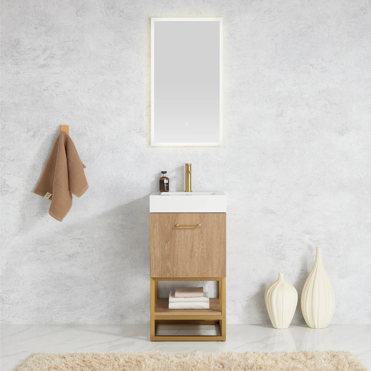 Room scene of a small vanity under a wall mirror, with a towel on a hook and cream vases on the floor