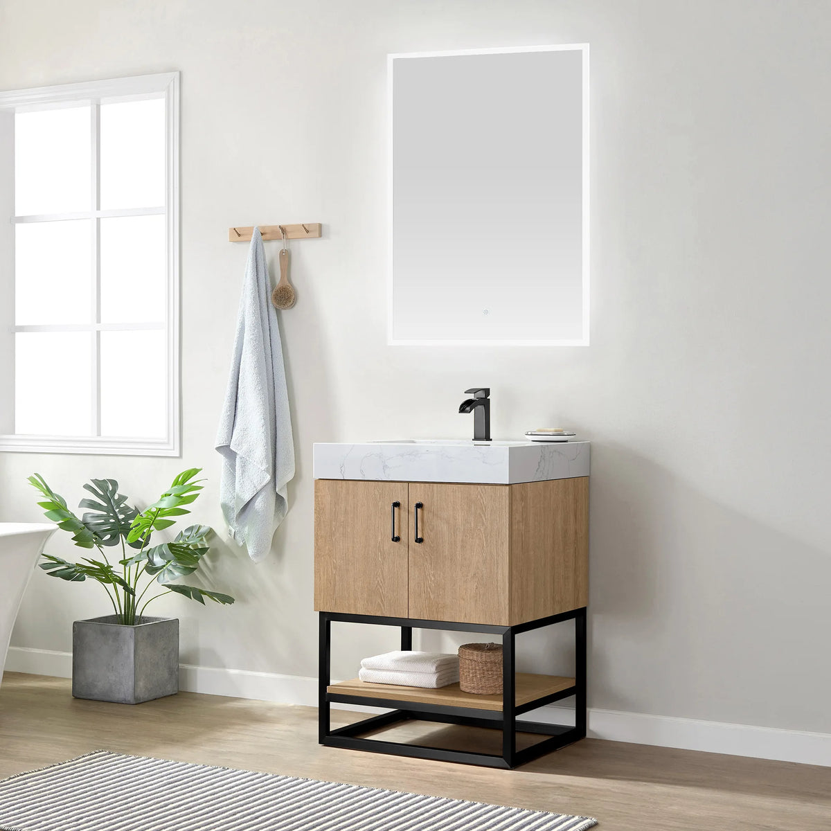 Wide room view of the vanity with its mirror, window, blue towel, wall rail and potted plant