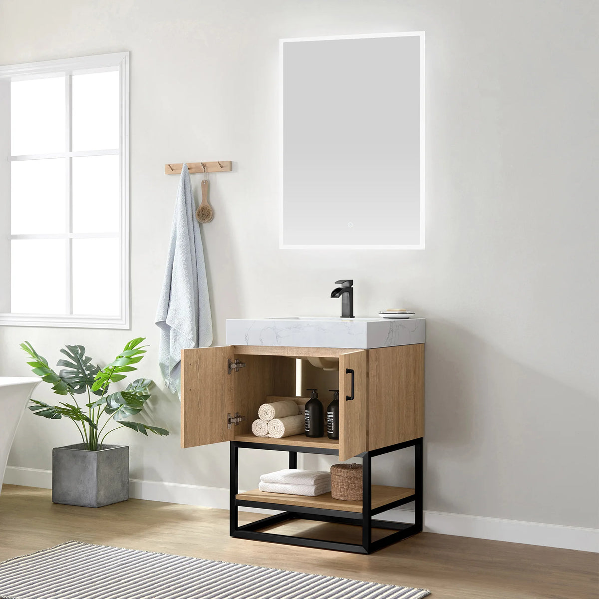 Door open on towels and a basket, with a potted plant and window behind the vanity