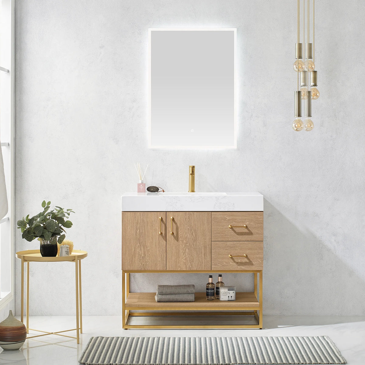 Room scene of the vanity under a lit mirror with pendant lights, a gold side table, plant and striped rug