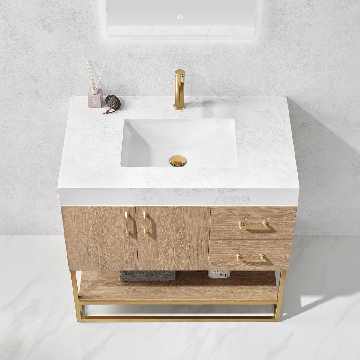 Overhead view of the white grain stone top with its undermount sink, a diffuser and gold pulls below