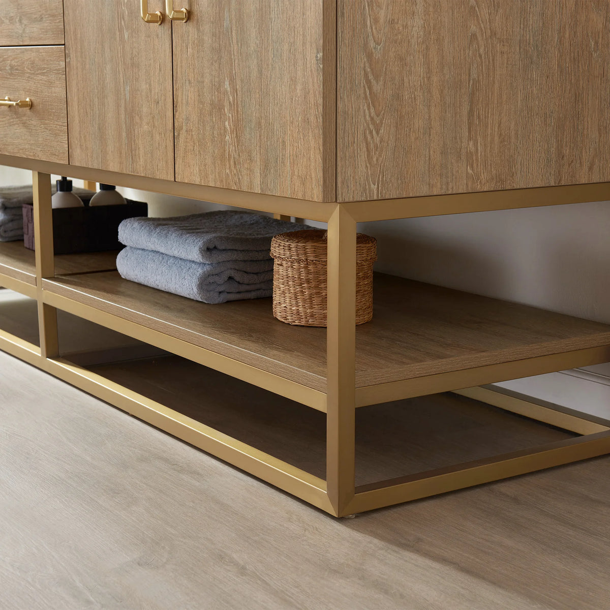 Low-angle detail of the open oak shelf with blue towels and a basket, set on a gold metal base
