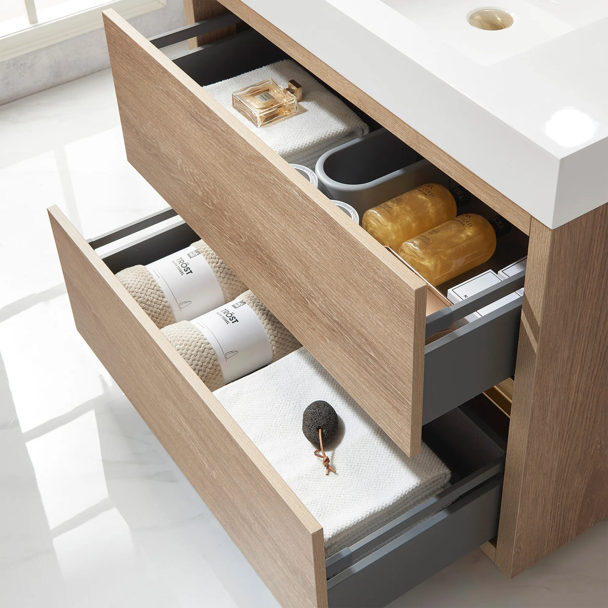 Close-up of open drawers with towels, amber jars and a sponge, gray drawer sides, oak fronts