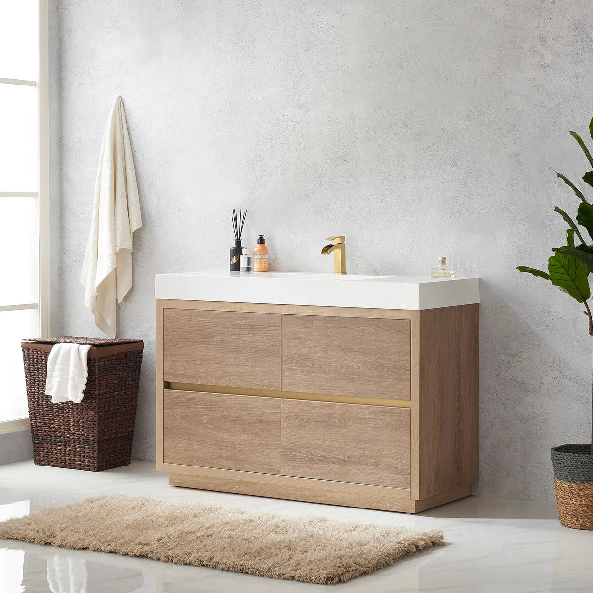 Angled view of the wide vanity with window, hamper, plant and rug in the room