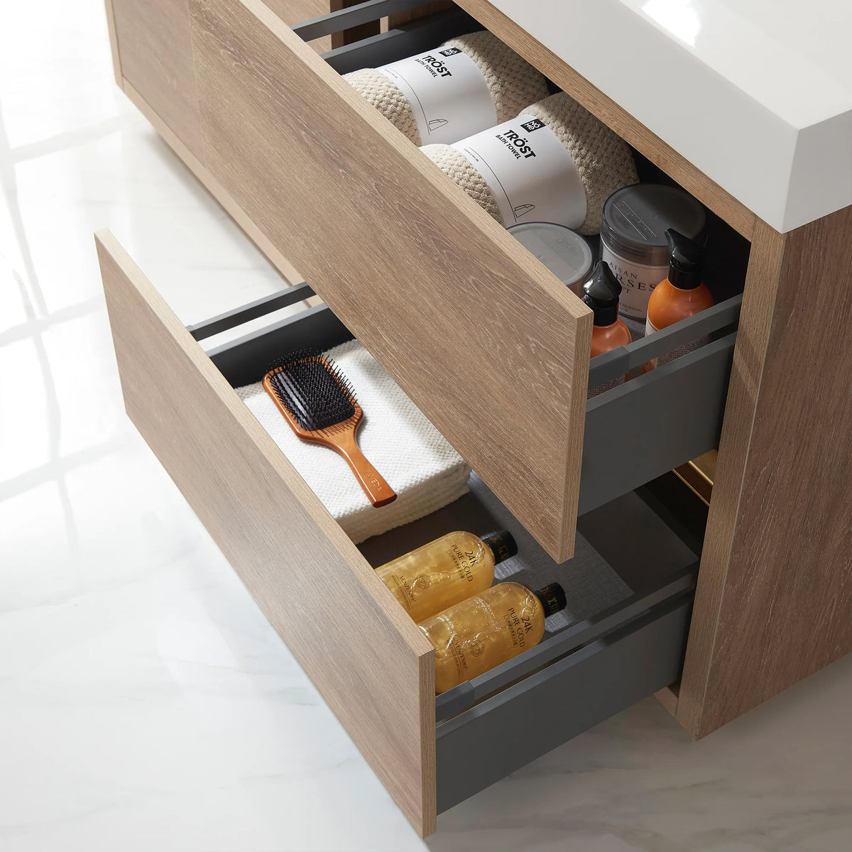 Close-up of an open drawer with towels, a hairbrush and bottles, oak front angled out