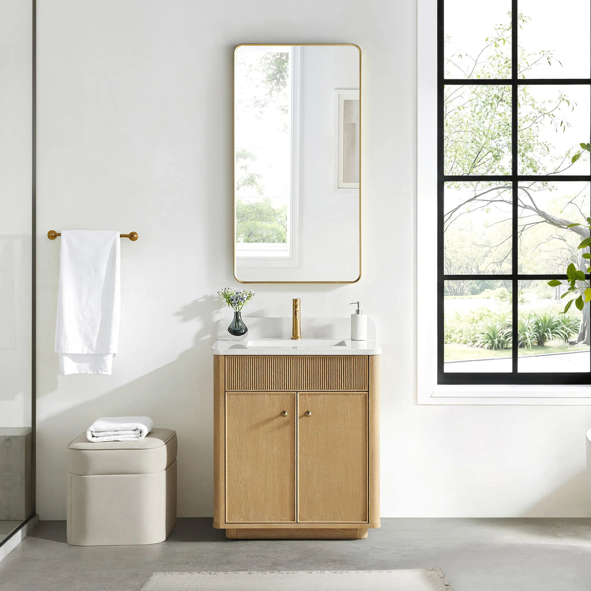 Matching tall rounded-rectangle gold mirror above the Washed Ash Grey vanity in a bathroom with a black-framed window