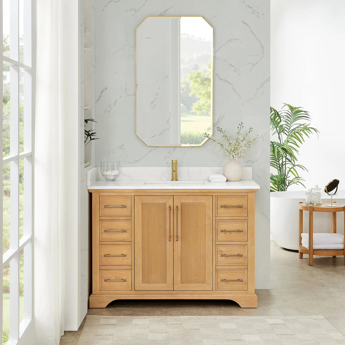 Room view: an octagonal mirror over a 48 inch single vanity in Oak Natural Brown, marble-look walls and tall windows