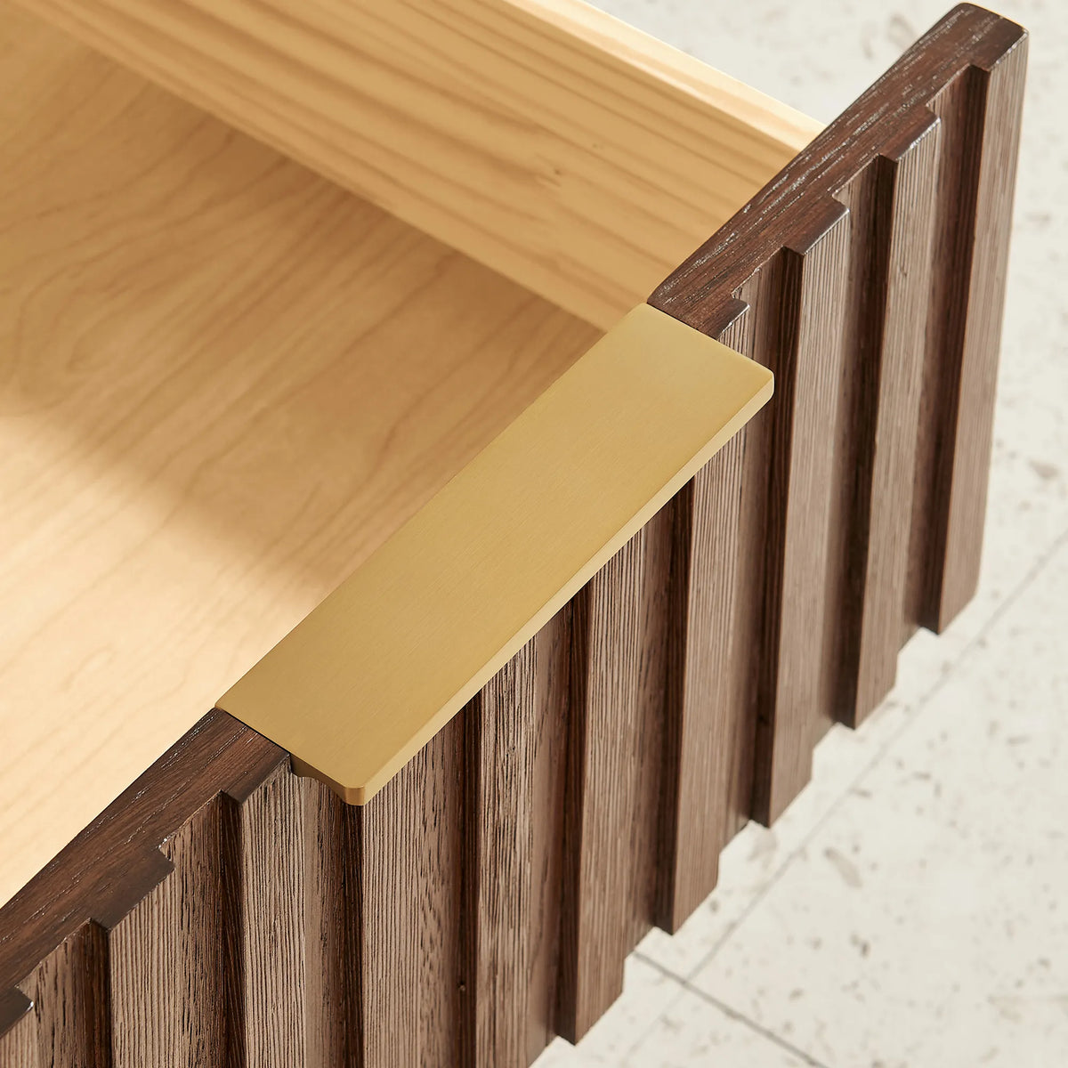 Detail of a gold pull against the grooved Aged Dark Brown Oak wood face of a 60-inch cabinet