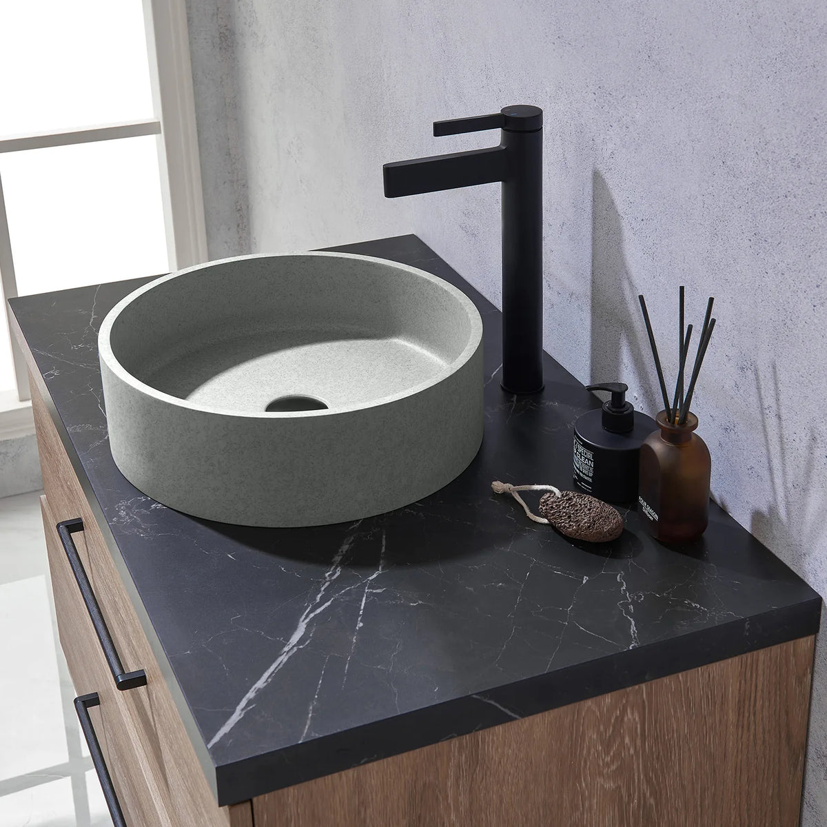 Tall black faucet rising next to the circular concrete vessel on a marbled black surface