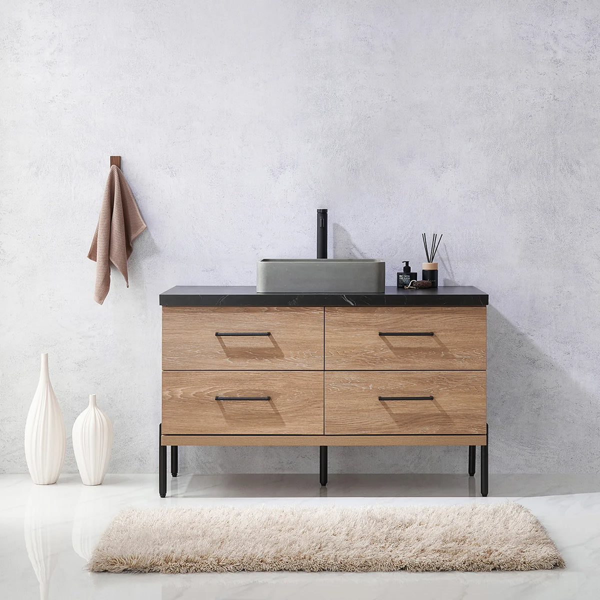 Pale plaster wall, white vases and a hanging towel behind the oak vanity on black legs